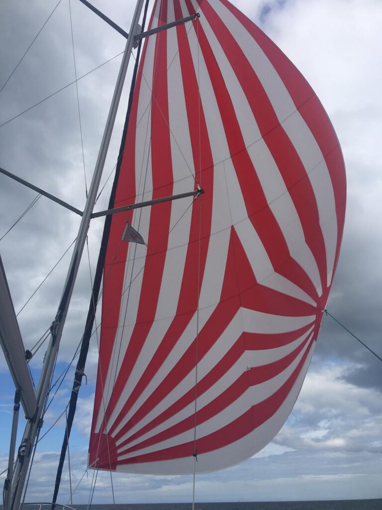 Red and white striped spinnaker made by Boatshed Sailmakers, flying from a yacht under a cloudy sky