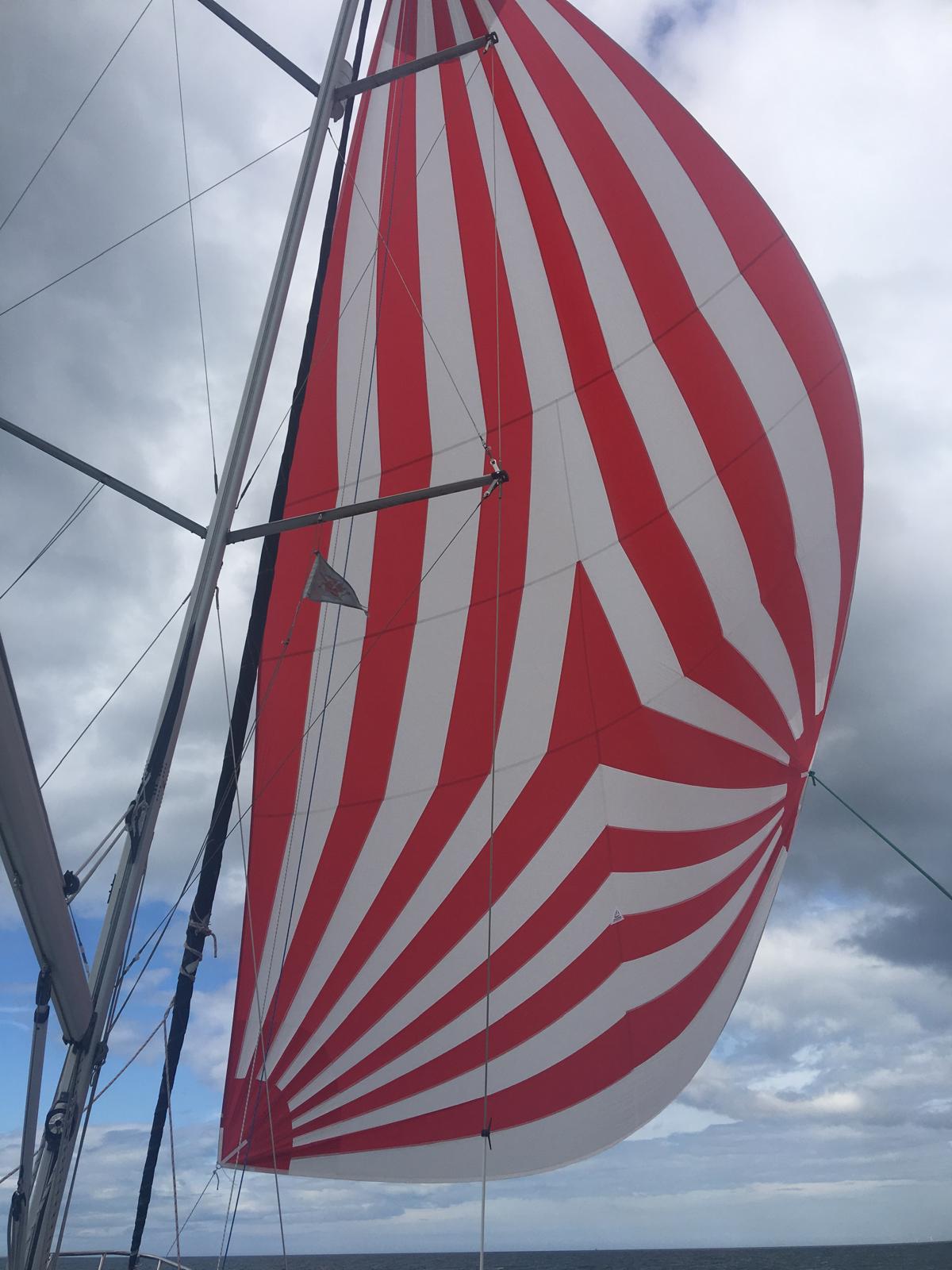 Red and white striped spinnaker made by Boatshed Sailmakers, flying from a yacht under a cloudy sky