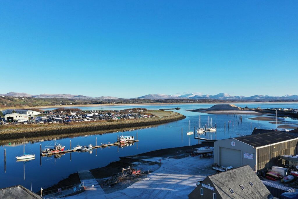 Aerial view of Pwllheli harbour and marina on a clear day, with the snow-capped mountains of Eryri in the distance