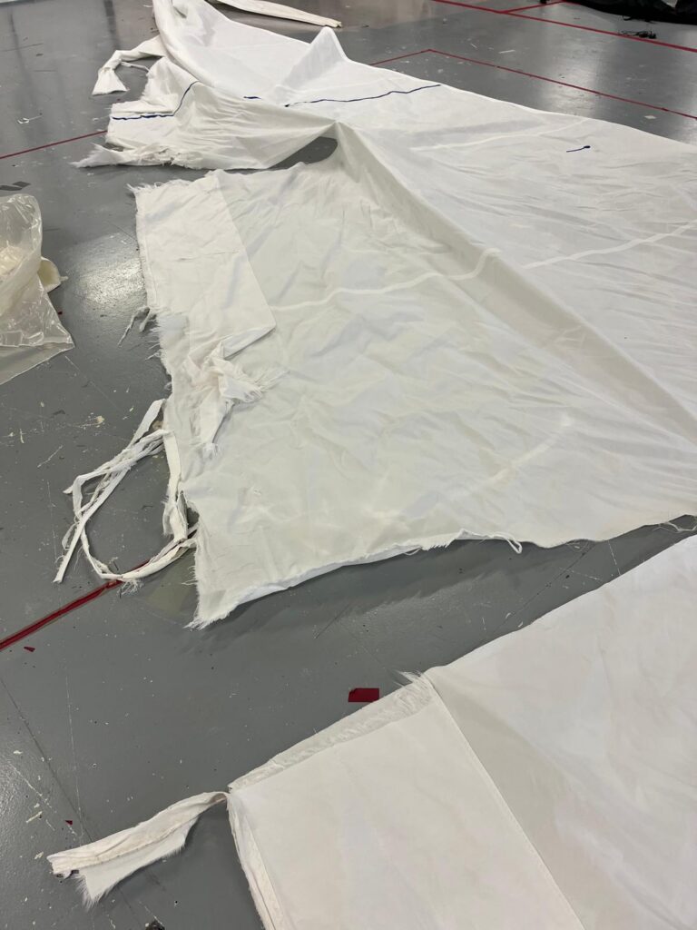 Torn white mainsail laid out on the loft floor at Boatshed Sailmakers, ready for repair