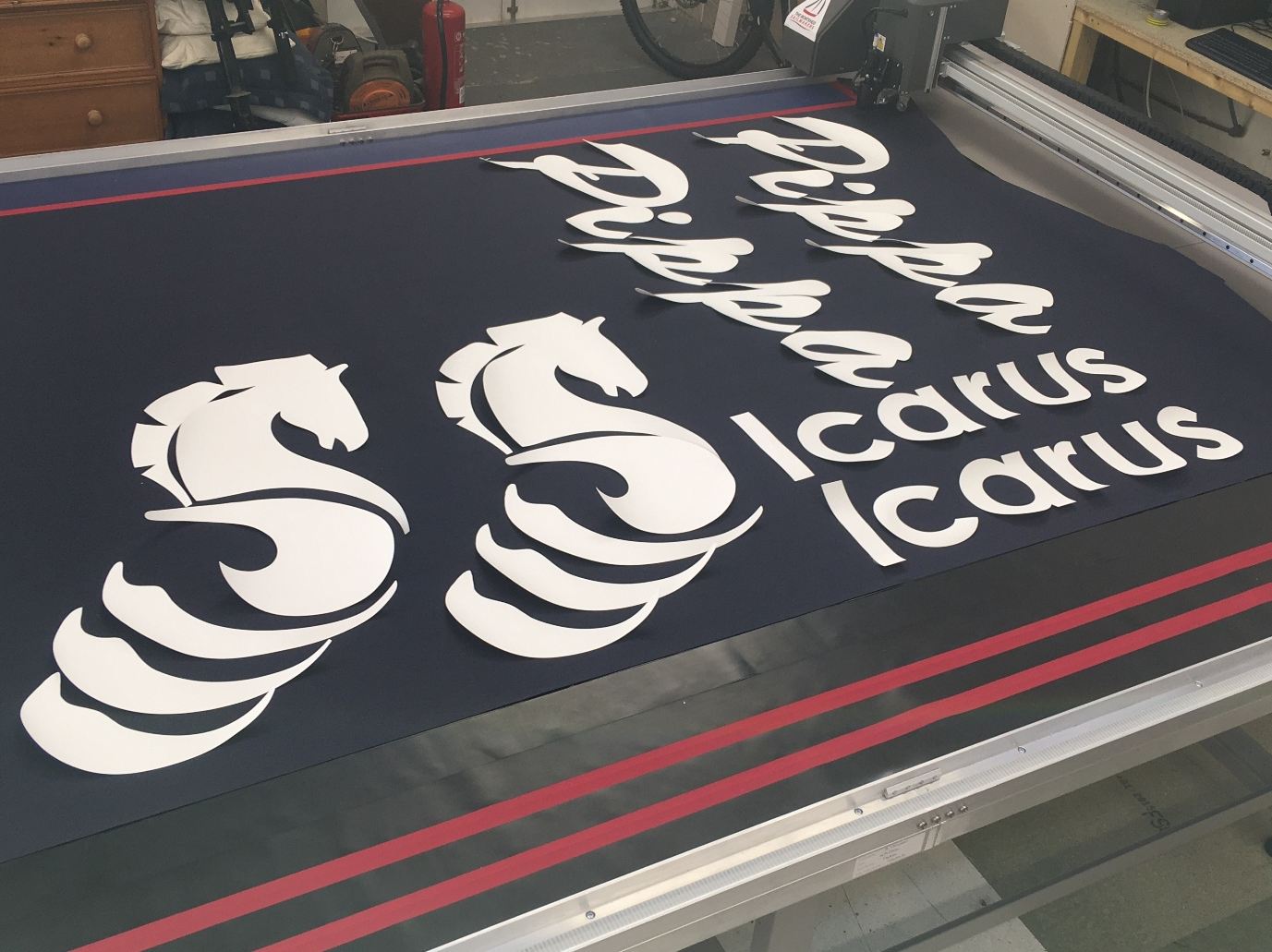 Pippa and Icarus boat name lettering with seahorse logos, digitally cut in white and laid out on navy canvas on the cutting table in our loft