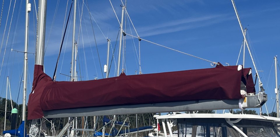 Burgundy lazy bag zipped closed over the mainsail along a yacht’s boom, with lazy lines running up to the mast