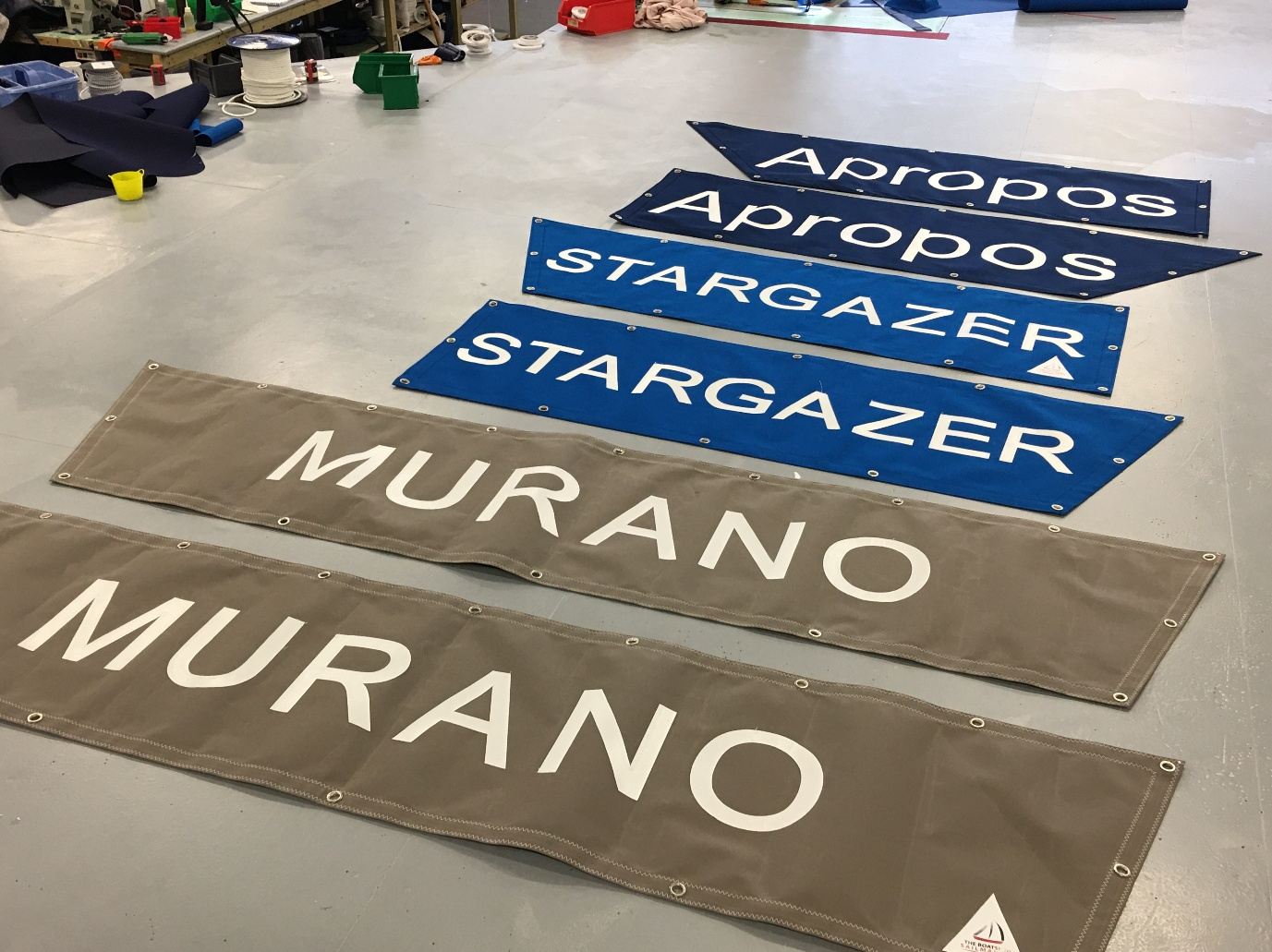Three pairs of made-to-measure spray dodgers in navy, blue and grey canvas, lettered Apropos, Stargazer and Murano, on the sail loft floor